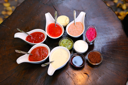 Various types of sauces are neatly arranged in small glass jars, showcasing vibrant colors and...