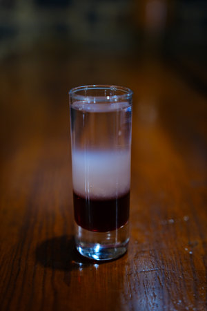 Colorful layered cocktail shot glass with orange, dark, and light layers surrounded by melting ice...