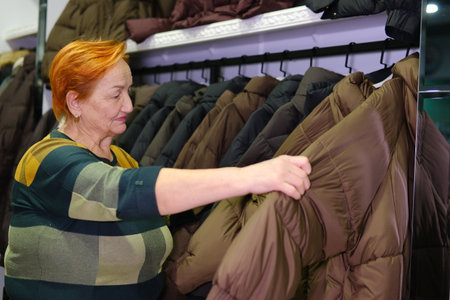 Selective woman choosing down jacket in clothing store with large assortmentの写真素材