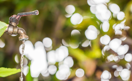 old and grunge brass faucet and water drop on green bokeh from tree background. Nature create water concept.の写真素材
