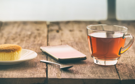hot tea cup with butter cake and smartphone on the table on the winter day, vintage toningの写真素材