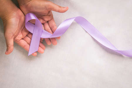Hands holding light purple ribbon on white fabric with copy space. Testicular Cancer Awareness, Alzheimer disease, Epilepsy awareness, World Cancer Day. Healthcare or hospital and insurance concept.の写真素材
