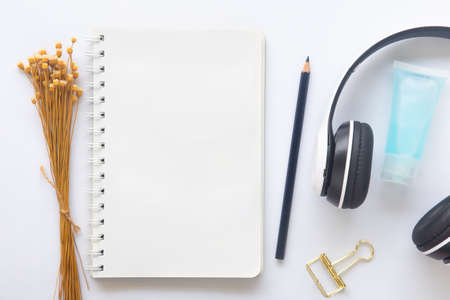 Blank white paper or notebook with copy space and pencil, hand sanitizer and head phone on white desk background. Concept to present new normal lifestyle activities post covid-19 pandemic.の写真素材