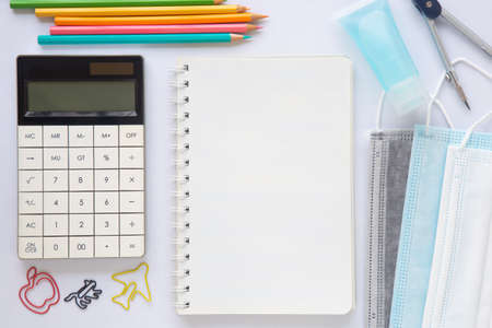 Blank white paper or notebook with stationary, mask and hand sanitizer on white background. Concept to present new normal lifestyle activities post covid-19 pandemic.の写真素材