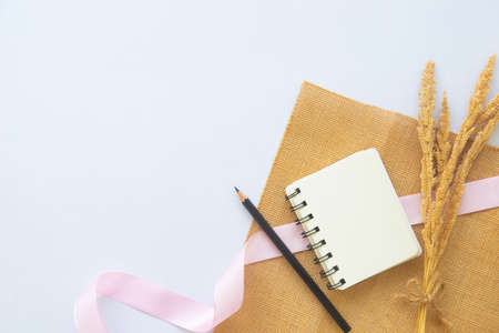 Blank white notebook with line or notepad and black pencil or pen near dried flower on white desk background with copy space in top view flat lay. Business, workplace, work space and education conceptの写真素材