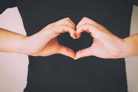 Woman wear black shirt and gesture hands for heart shape. Concept for love, help, kindness, donate, heart health, mental healthcare, medical, positive thinking and insurance and csr business plan.の写真素材