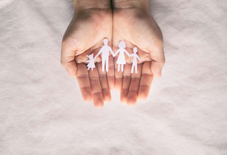Hand holding family paper cut on fabric background. Family day concept, foster care, domestic violence, homeschool, international day of families, world mental health day, world autism awareness day.の写真素材