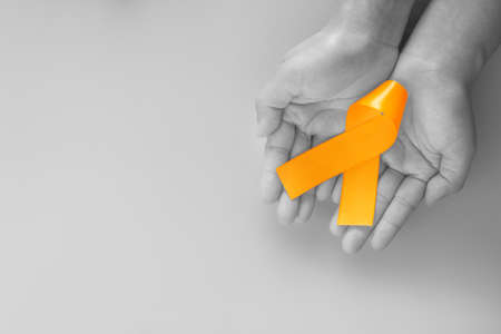 Hands holding orange color ribbon on  black and white with copy space. Kidney Cancer Awareness,...
