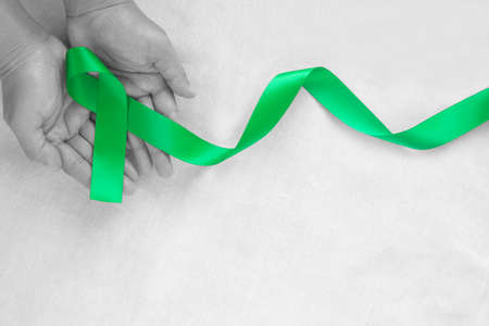 Hand holding Emerald green or jade green ribbon curl on white fabric background with copy space, symbol for Liver Cancer awareness, World Cancer Day. Healthcare or hospital and insurance concept.の写真素材