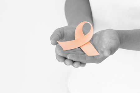 Hand holding Peach color ribbon curl on white fabric background with copy space, symbol for Uterine and Endometrial cancer awareness, World Cancer Day. Healthcare or hospital and insurance concept.の写真素材