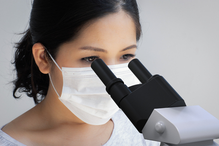 Asian scientist wearing face mask and looking at microscope