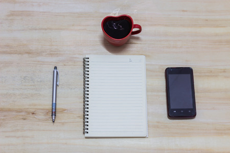 Blank cell phone, cup of coffee and diary on a wooden tableの写真素材