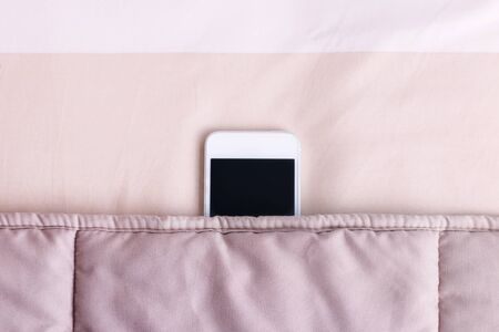 Mobile phone under blanket in bedroom.の写真素材
