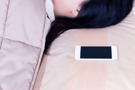 Women sleeping with mobile phone in bedroom.の写真素材