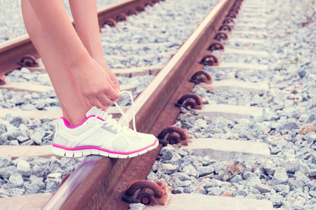 Young woman tying shoelaces on the rail of the railway.
