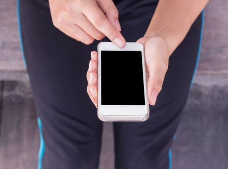 Young woman sitting on old wooden floor with hands holding smartphone with blank screen.