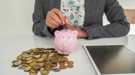 A business successful person is putting the coins in piggy bank while working in the office. saving...