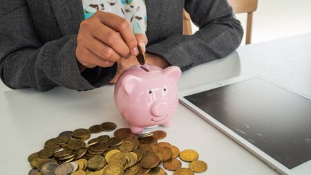 A business successful person is putting the coins in piggy bank while working in the office. saving money is an investment for the future. Banking investment.の写真素材
