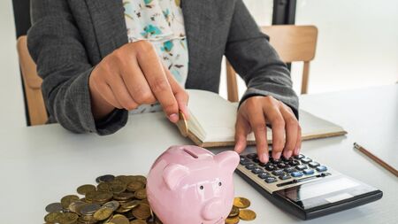 A business successful person is putting the coins in piggy bank while working in the office. saving money is an investment for the future. Banking investment.の写真素材