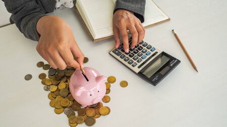 A business successful person is putting the coins in piggy bank while working in the office. saving money is an investment for the future. Banking investment.の写真素材