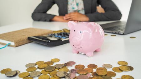 A pink piggy bank in office with successful business women is working background. saving money is investment. saving money for business investment.の写真素材