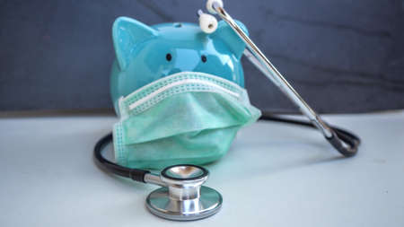 Stethoscope and Piggy Bank Wearing Protective Medical Face Mask, isolated on white background.