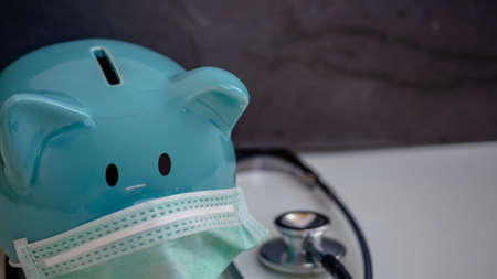 Stethoscope and Piggy Bank Wearing Protective Medical Face Mask, isolated on white background.