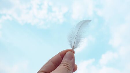 Bird feather in a hand in abstract groups of stratus clouds height in the sky. Stunning springtime...