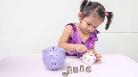 Three years old child is saving money into piggy bank. in white background. saving money for future, dream, education. happy child. stay at home. family activities.の写真素材