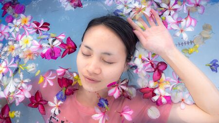 A woman soaking in the water with flowers in swimming pool.  taking care, spa and relaxation. taking...