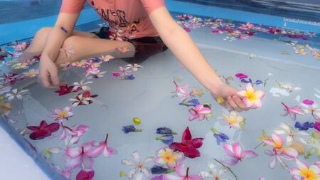 A woman soaking in the water with flowers in swimming pool.  taking care, spa and relaxation. taking holiday concept.の写真素材