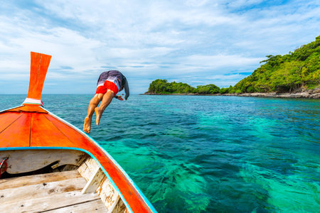 Young man jumping into the sea from longtail boatの写真素材