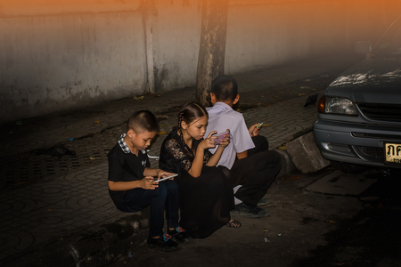 THAILAND,BANGKOK  - OCTOBER 4: One girl and two child sit play mobile phone at wayside on October 4,2017 in Bangkok,THAILAND.のeditorial素材