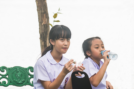 SAMUTPRAKAN - OCTOBER 26 : Two students girl sit on bench in public garden eat something on October 26, 2017 in  Samutprakan province, Thailand.のeditorial素材