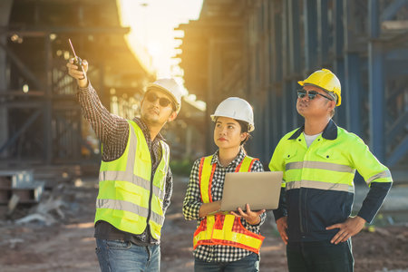 An Asian Team of Engineers and Foremen Inspect Objects at the Construction Site of New Concrete...