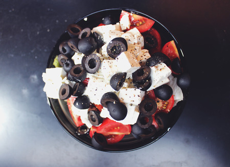Greek salad with sirtaki cheese and black olives and a red tomato. On white cheese is ground pepper.