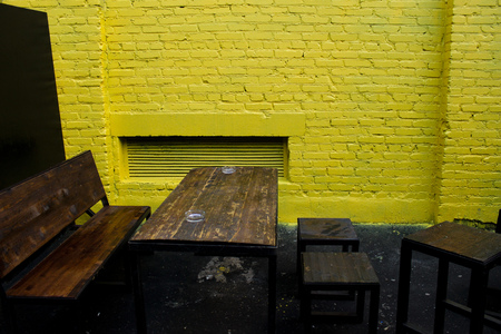 A wooden bench with a wooden table against a yellow brick wall.