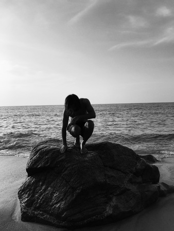 Silhouette of a guy with long hair posing on a large stone on the background of the sea the image is similar to Tarzan or Mowgliの写真素材