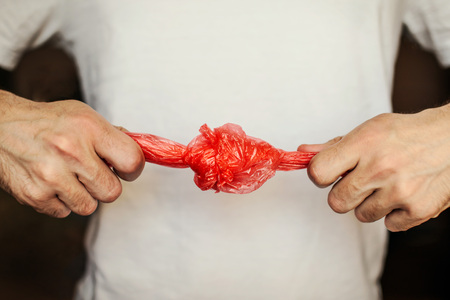A red plastic bag is knotted by a man's hand to throw it out.の写真素材