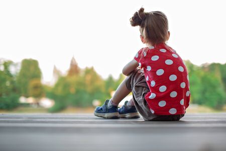 Girl sitting back on the pier looks into the distance and dreamsの写真素材