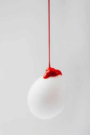 Red color paint flowing on white egg, concept Easter painted eggsの写真素材