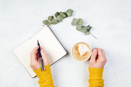 Hand and cup of coffee, woman writes a note and drinks coffee, white color background