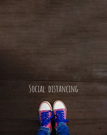 Legs in bright sneakers on wooden background. Social distancing, concept of staying physically apart for control spread of COVID-19の写真素材