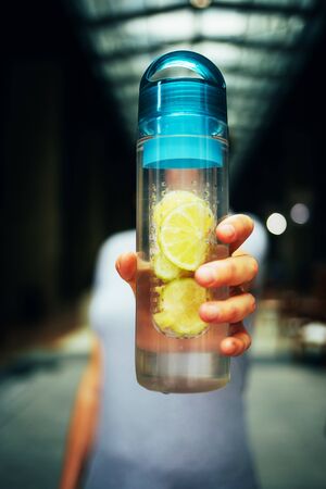 Female hand holds a bottle with detox drink lemon on a background cityの写真素材