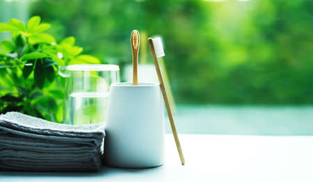 Two bamboo toothbrushes in a cup, glass with water and grey towelsの写真素材
