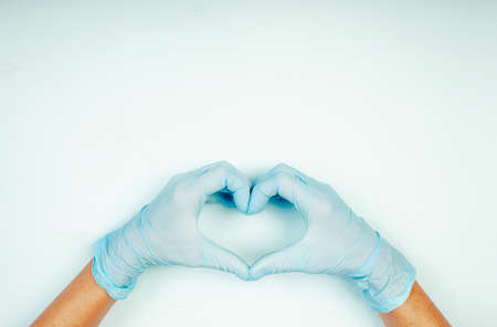 Hands in heart-shaped medecine gloves on blue background