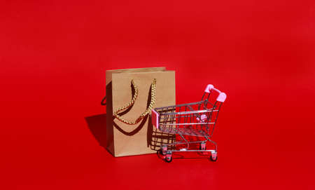 Shopping cart and paper bag for purchases on red background with space for text. Black Friday conceptの写真素材