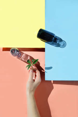 A womans hand holding a leaf of a plant and two bottles, top view