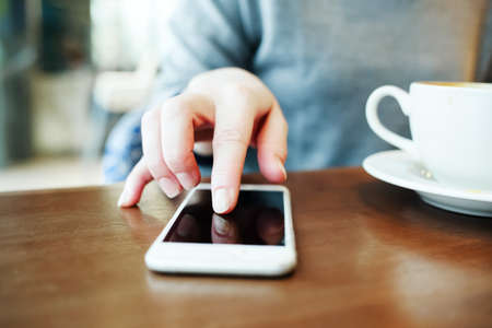 Woman working on a smartphone in a cafe and drinks coffee