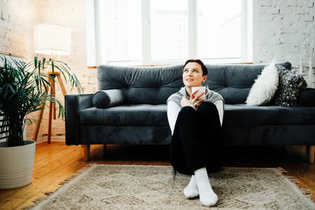 A woman sits on the floor of the house, dreams and coffee, calm day at home